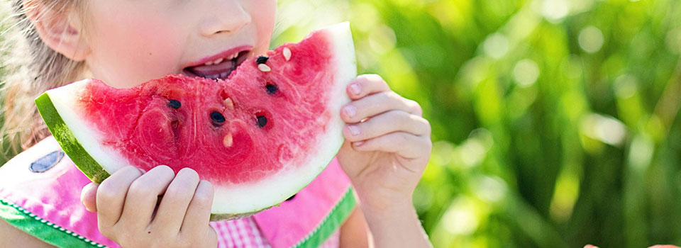 Closeup of girl wearing pink dress eating a slice of watermelon