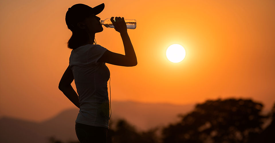 silhouette of woman drinking from a water bottle with a bright orange sky in the background silhouette of woman drinking from a water bottle with a bright orange sky in the background