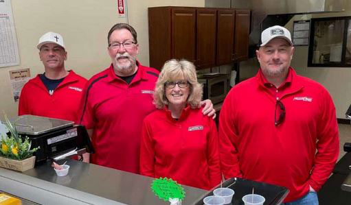 Four people in red shirts standing behind meat counter