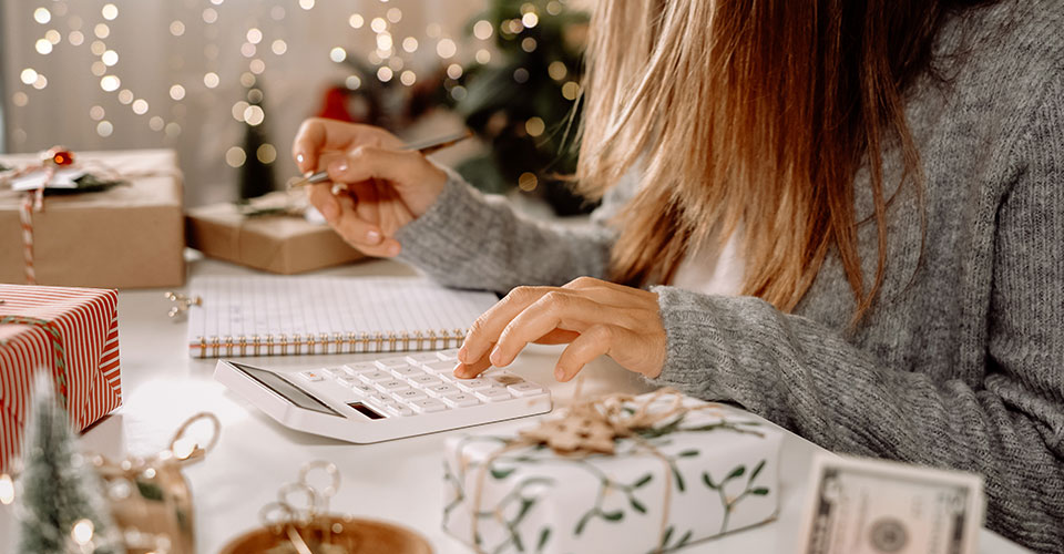 Closeup photo of woman using a calculator to figure a family budget, with holiday gifts in the background