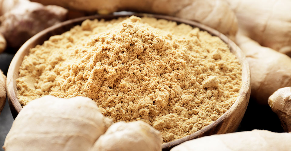 closeup of whole ginger surrounding a bowl of ground ginger
