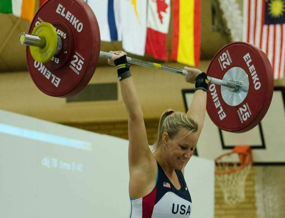 Woman wearing a jersey that reads USA and holding weight bar with heavy weights above her head