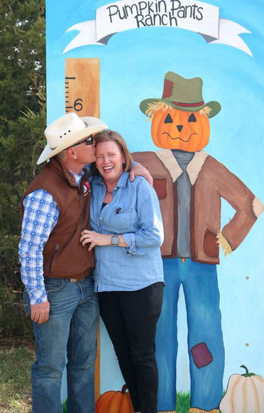Man in cowboy hat kissing a woman in front of a painting of a cartoon figure with pumpkin head