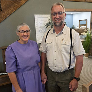 Woman and man dressed in Amish-style clothing standing and smiling at camera