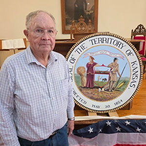 elderly man standing in museum next to the original state seal of kansas