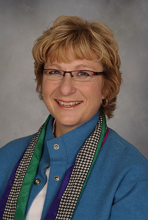 Portrait of a woman with medium-length light hair wearing eyeglasses and a blue shirt smiling at the camera