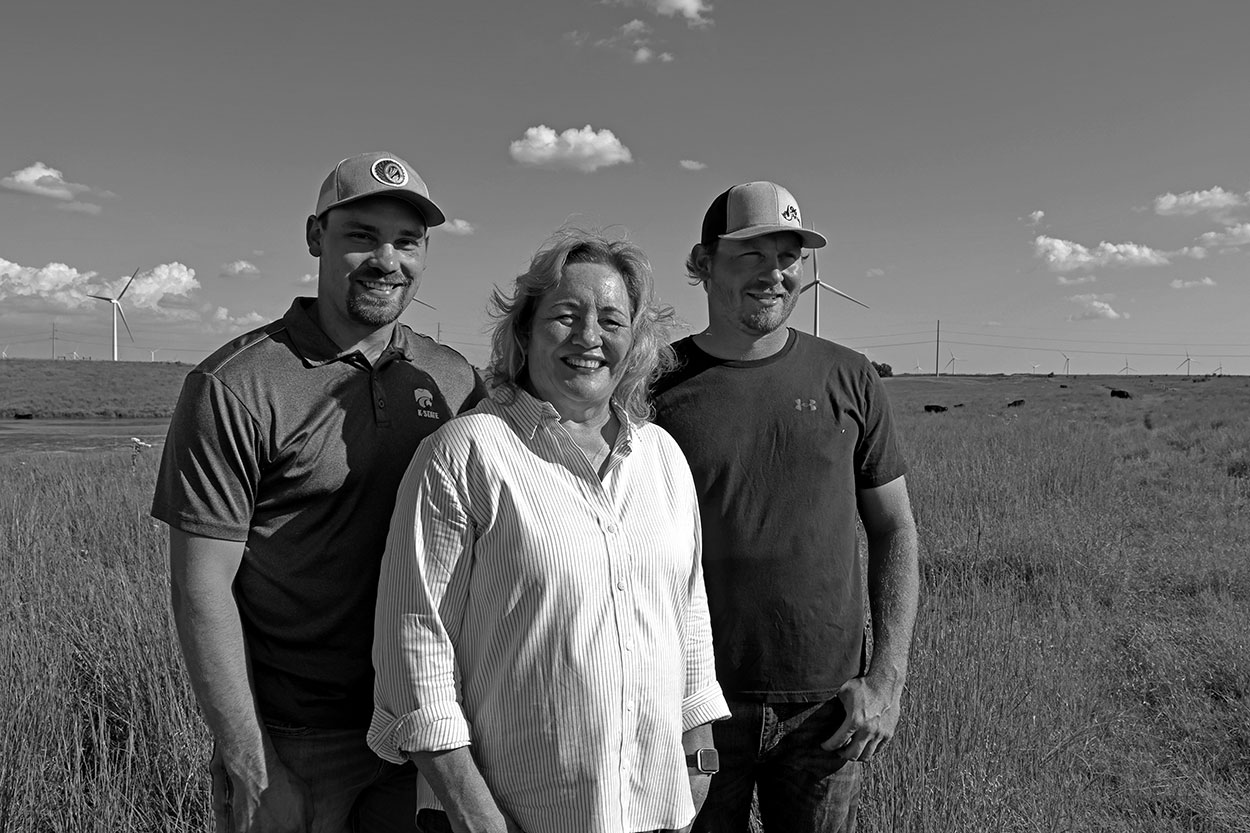 Woman standing in front of two young men in farm field and clear sky in the background