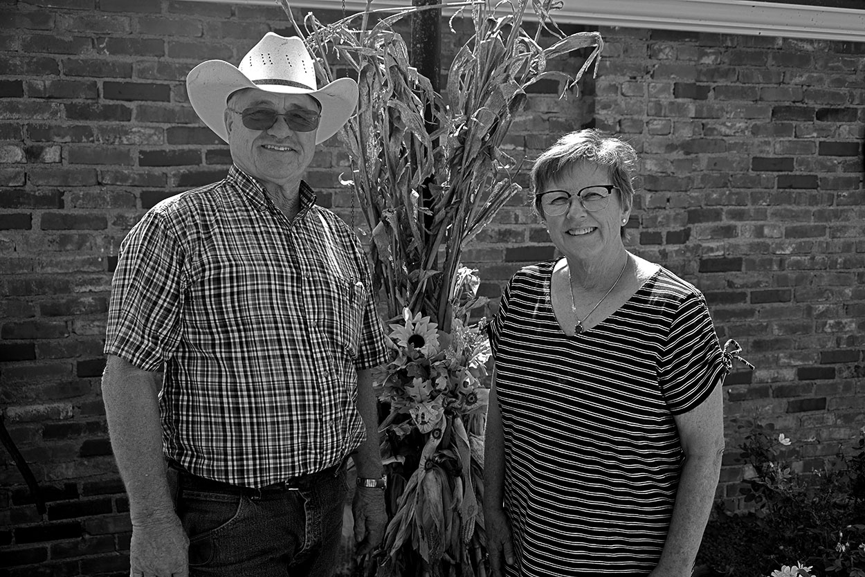 Man wearing cowboy hat and woman with white shirt standing in front of brick home