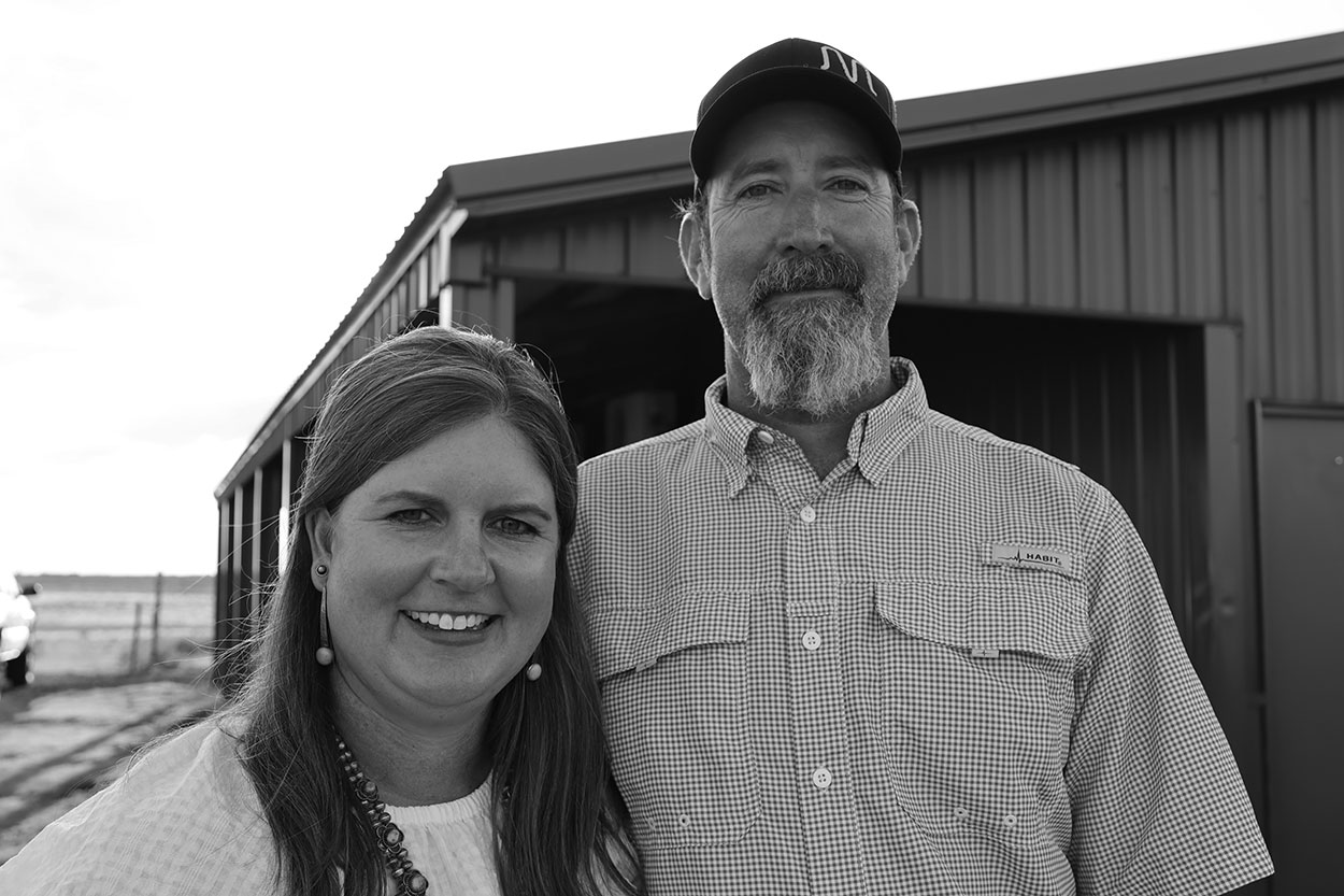 Woman with long hair and man with beard standing in front of barn