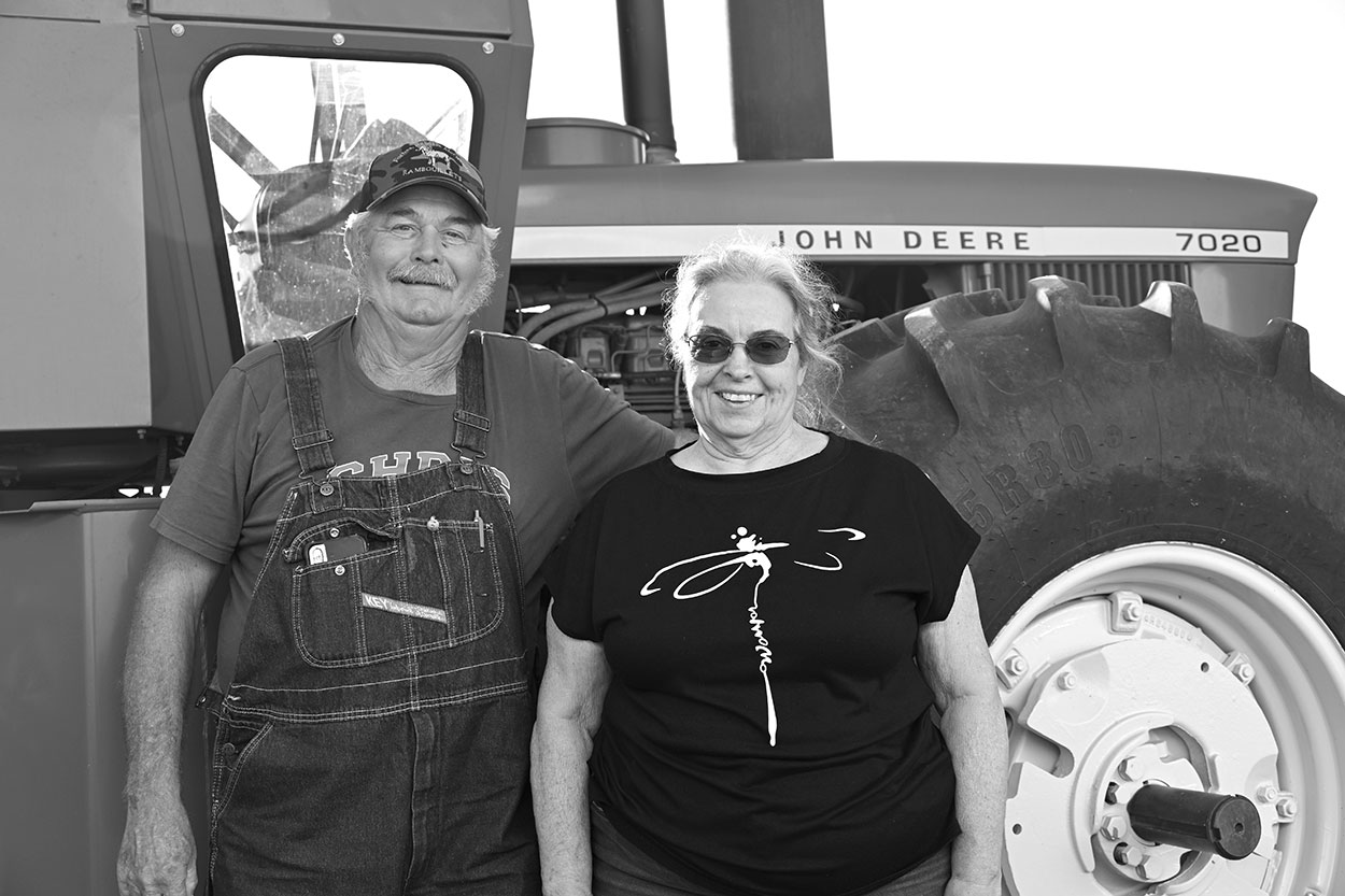 Man in overalls and woman standing in front of a farm tractor