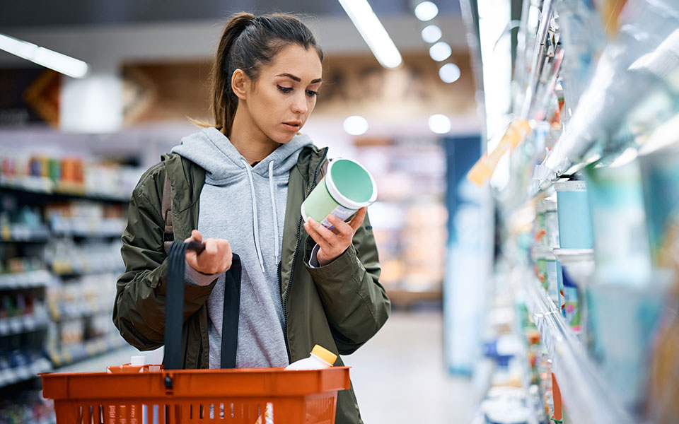 Woman in grocery store aisle reading the nutrition label on a product from the shelf