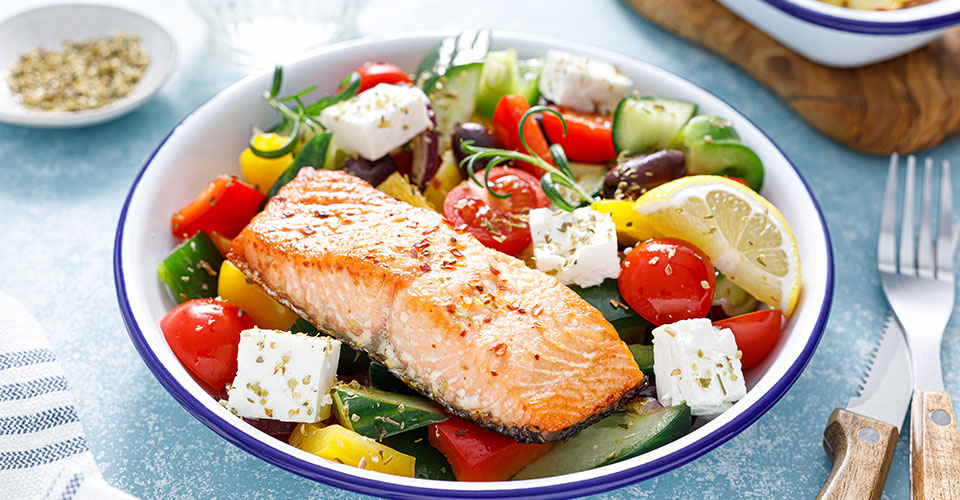Closeup image of a white plate with a piece of salmon and numerous salad vegetables