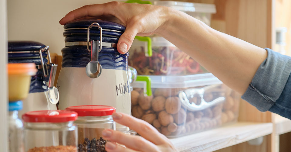 closeup of woman's hand grabbing glass container on a pantry shelf