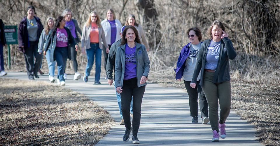 Several women walking down a paved trail wearing shirts that read 'Walk Kansas'