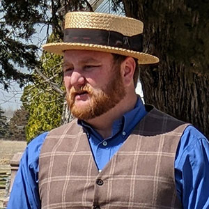 picture of man wearing a checkered shirt and flat-brim hat, looking right to left in the picture