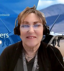 Woman wearing glasses, headphones and black shirt, smiling at camera