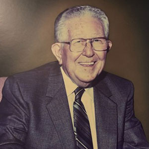 Portrait of older man with eyeglasses and gray hair wearing a black suit and smiling at the camera