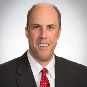 portrait of man wearing dark suit and red tie, smiling at the camera