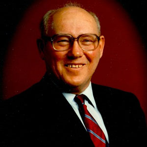 Portrait of man with balding hair wearing a black suit and red tie smiling at the camera