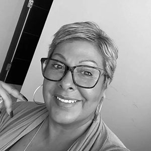 Woman with dark hair wearing glasses and smiling at camera