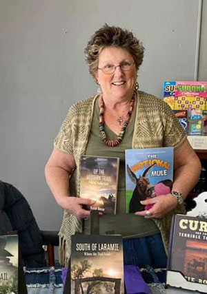 Woman standing and smiling at camera while holding books in each arm