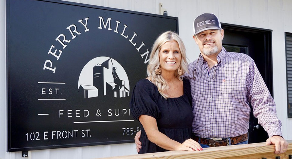 Woman and man with arms around eachother standing in front of black sign that reads Perry Milling