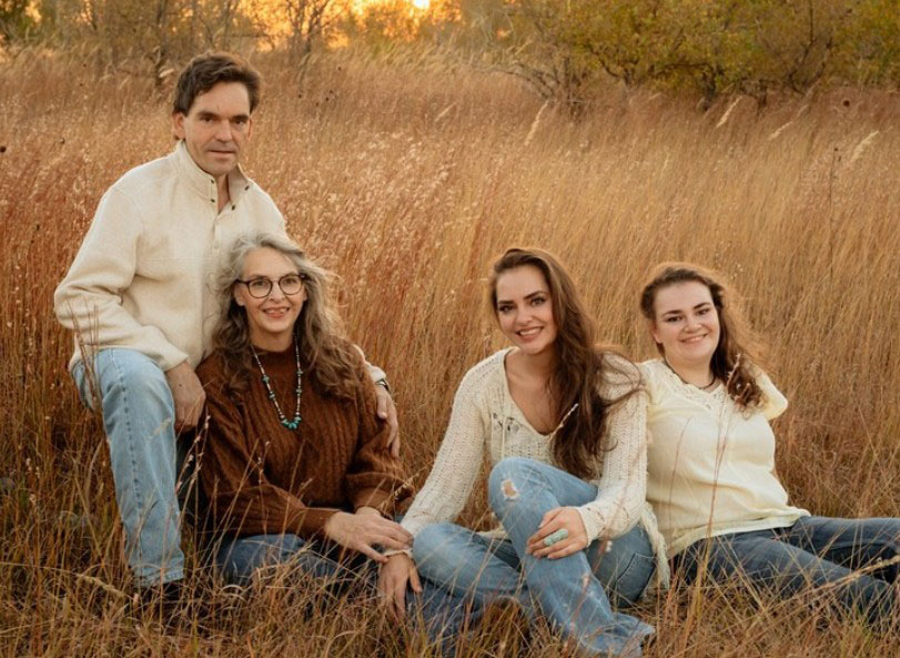 Family portrait including man in white shirt, woman leaning against him, and two younger women sitting in grassy field