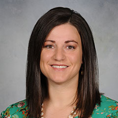 Portrait of woman with black hair wearing a green shirt and smiling at the camera