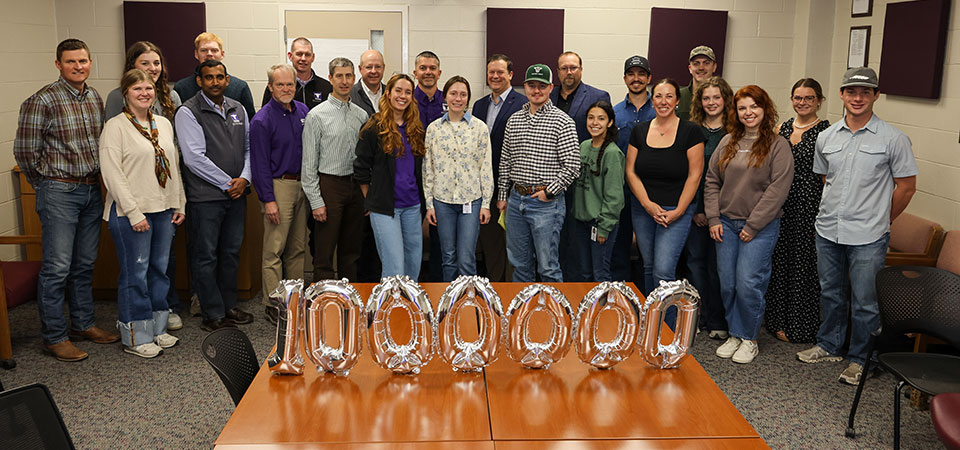Group of more than a dozen people stand in front of a table that holds a mylar balloon in the shape of the number one million