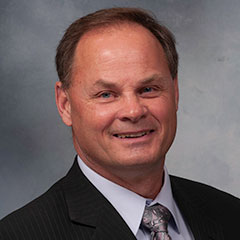 Portrait, Chris Onstad smiling at camera and wearing a dark suit