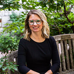 Woman wearing eyeglasses and black shirt sitting in front of a background of lush, green leaves