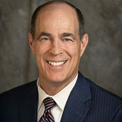 Picture of balding man smiling at camera and wearing a dark suit with tie